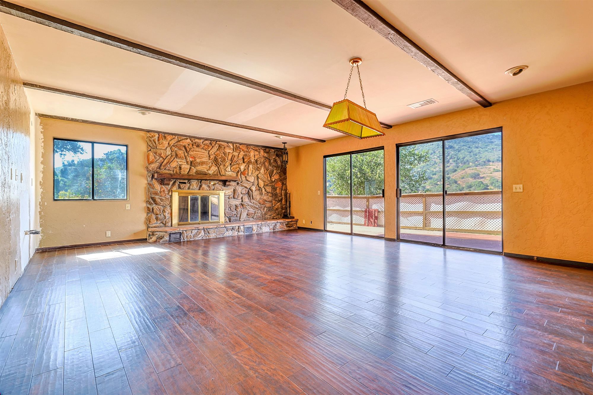 Room at 8257 Camp Chaffee Rd with exposed ceiling beams, a stone-faced fireplace and sliding doors to the terrace